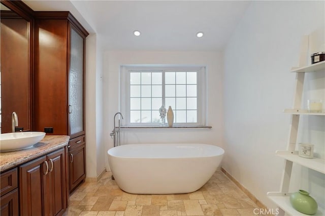 full bath featuring recessed lighting, stone finish floor, vanity, a freestanding tub, and baseboards