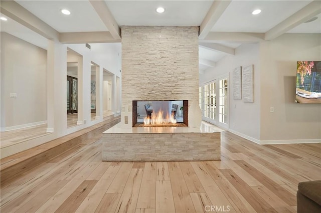 interior space with recessed lighting, a stone fireplace, light wood-type flooring, beamed ceiling, and baseboards