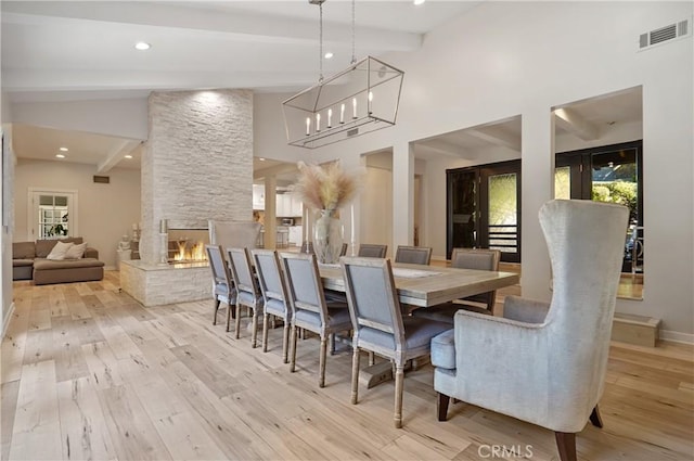 dining space featuring visible vents, light wood-style floors, a stone fireplace, beamed ceiling, and baseboards