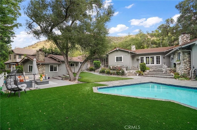 rear view of house featuring a patio, a yard, a chimney, and an outdoor pool