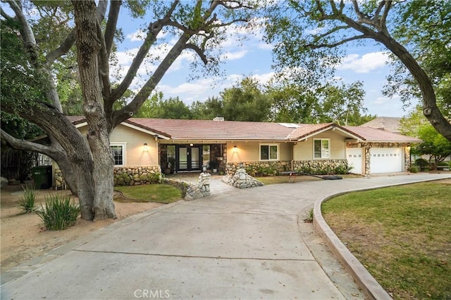 ranch-style home with an attached garage, stone siding, concrete driveway, and a front yard