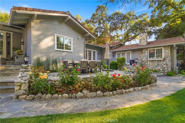 back of property featuring stone siding, a chimney, and a patio