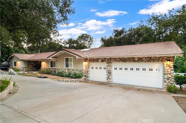 ranch-style home featuring a garage, stone siding, a tile roof, and driveway