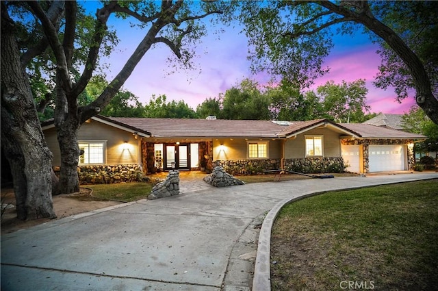 single story home with driveway, stone siding, a garage, and a yard