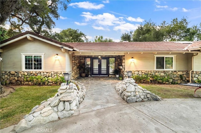 single story home featuring stone siding, french doors, a front lawn, and a tile roof