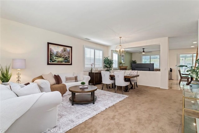 carpeted living room with ceiling fan with notable chandelier