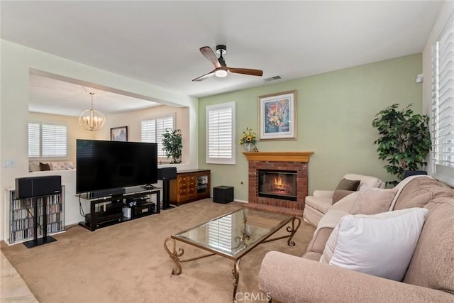 living room featuring light colored carpet, a fireplace, and ceiling fan with notable chandelier