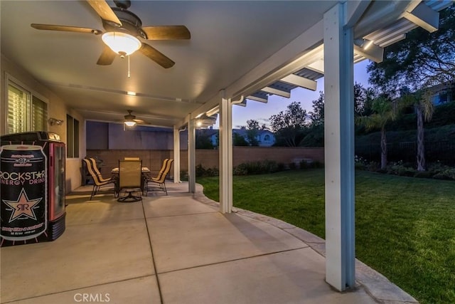 patio terrace at dusk featuring ceiling fan and a yard