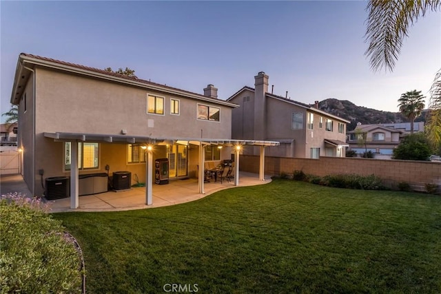 back house at dusk featuring central air condition unit, a patio area, and a yard