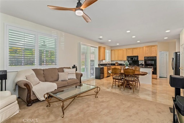 living room featuring ceiling fan, sink, light colored carpet, and a healthy amount of sunlight