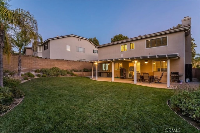 back house at dusk with a lawn and a patio