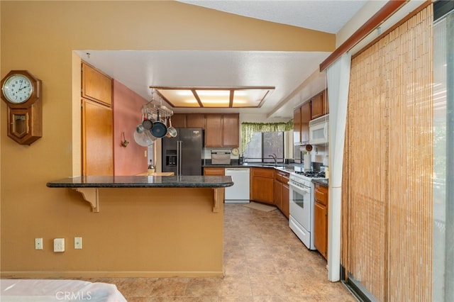 kitchen featuring a breakfast bar, kitchen peninsula, sink, white appliances, and dark stone counters