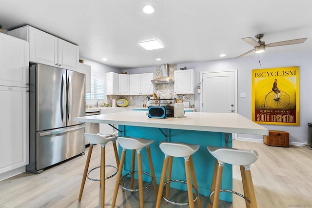 kitchen featuring a kitchen island, stainless steel refrigerator, white cabinetry, a breakfast bar area, and wall chimney exhaust hood