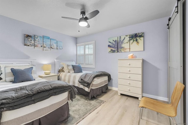 bedroom with ceiling fan, light hardwood / wood-style floors, and a barn door