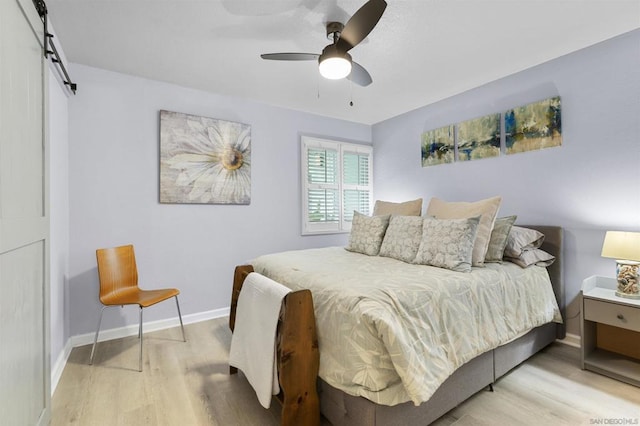 bedroom with ceiling fan, a barn door, and light wood-type flooring