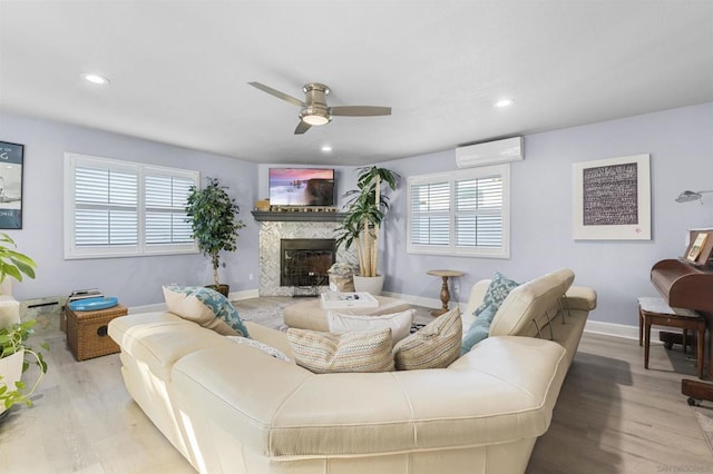 living room with a wall unit AC, ceiling fan, a fireplace, and light hardwood / wood-style flooring