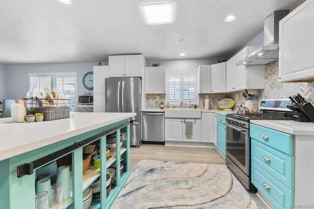 kitchen featuring appliances with stainless steel finishes, wall chimney range hood, blue cabinetry, and white cabinetry