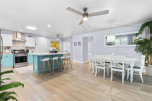 kitchen featuring stainless steel range, ceiling fan, a kitchen breakfast bar, wall chimney exhaust hood, and white cabinets