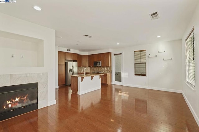 kitchen with a kitchen bar, an island with sink, stainless steel appliances, tasteful backsplash, and a fireplace