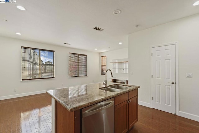 kitchen featuring light stone countertops, dishwasher, dark wood-type flooring, an island with sink, and sink