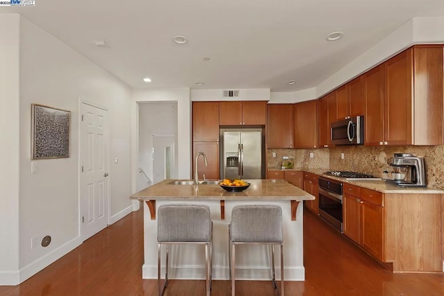 kitchen with a kitchen bar, appliances with stainless steel finishes, tasteful backsplash, a kitchen island with sink, and sink