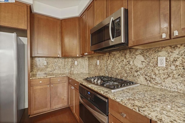 kitchen with stainless steel appliances, decorative backsplash, and light stone counters