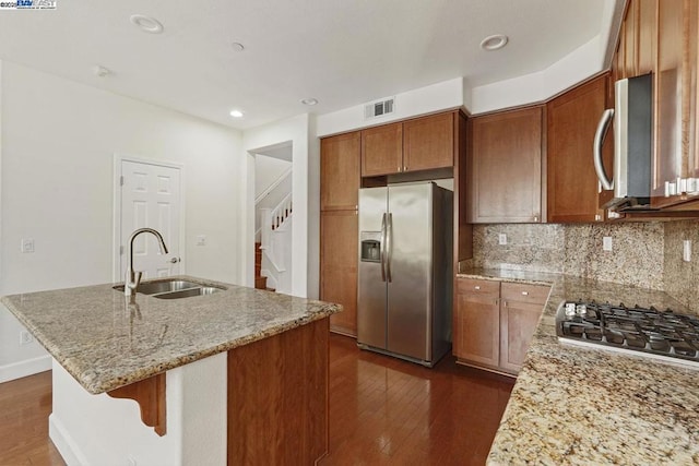 kitchen featuring appliances with stainless steel finishes, dark hardwood / wood-style flooring, sink, light stone counters, and a center island with sink