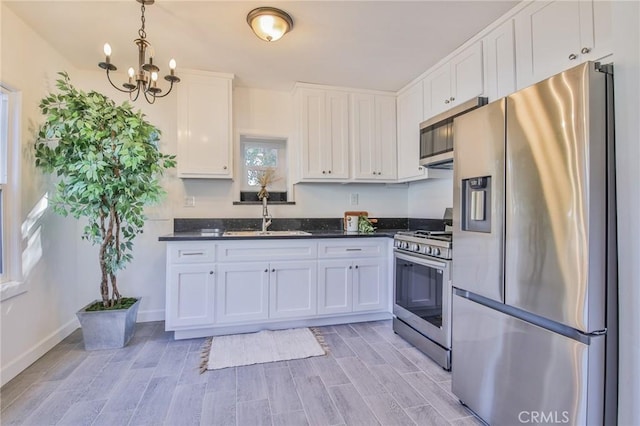 kitchen featuring decorative light fixtures, a notable chandelier, sink, stainless steel appliances, and white cabinets