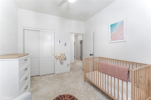 carpeted bedroom with ceiling fan, a nursery area, and a closet