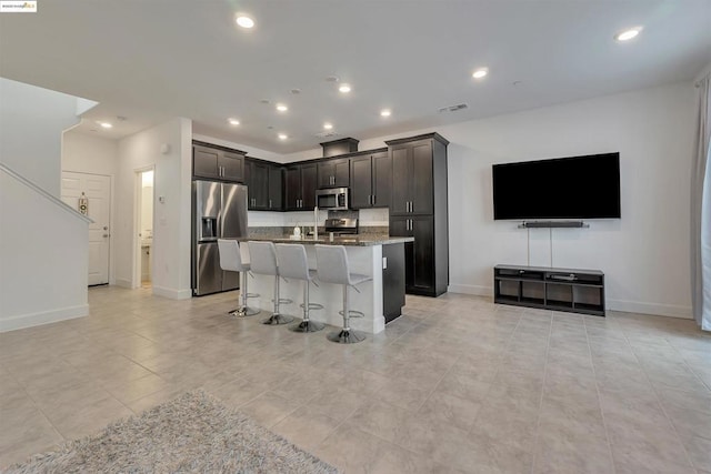 kitchen with light stone countertops, an island with sink, a breakfast bar area, stainless steel appliances, and light tile patterned floors