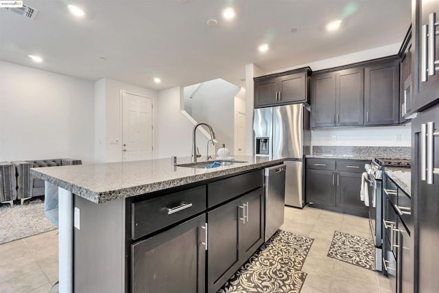 kitchen featuring dark brown cabinetry, stainless steel appliances, an island with sink, sink, and light tile patterned flooring