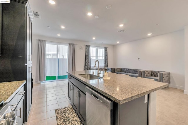 kitchen with dishwasher, sink, light tile patterned flooring, a kitchen island with sink, and light stone countertops