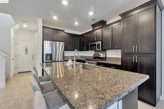 kitchen with a kitchen island with sink, sink, stainless steel appliances, and dark brown cabinetry