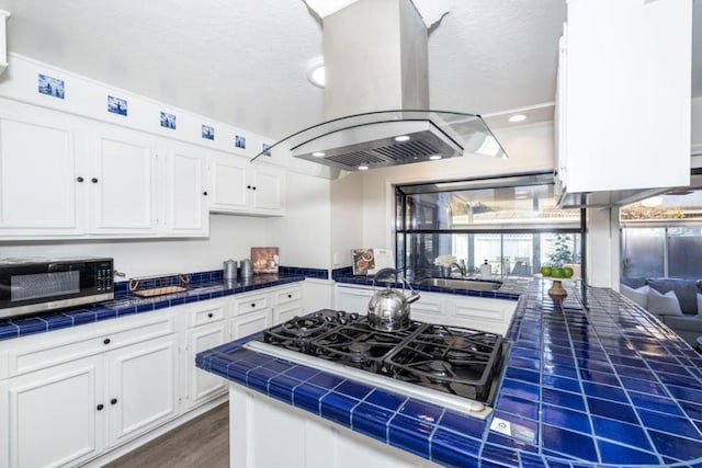 kitchen featuring sink, island range hood, tile countertops, gas cooktop, and white cabinets