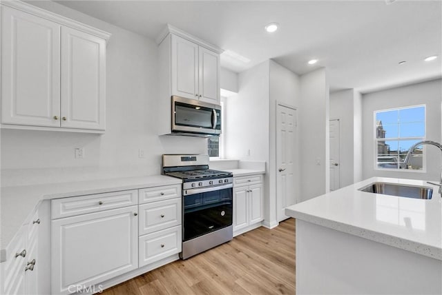 kitchen with appliances with stainless steel finishes, sink, white cabinetry, and light hardwood / wood-style floors