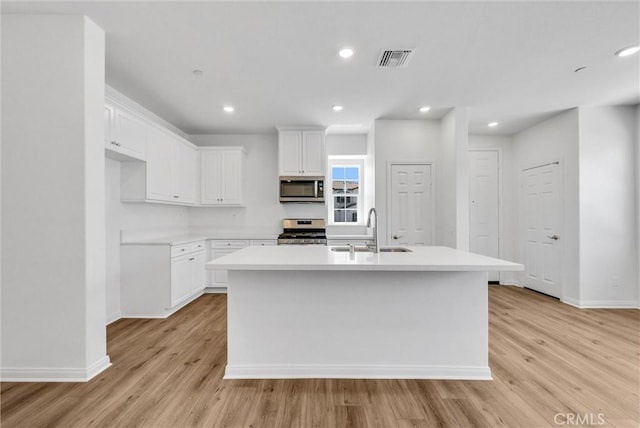 kitchen featuring sink, light wood-type flooring, an island with sink, stainless steel appliances, and white cabinets