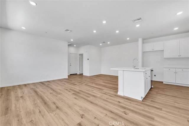 kitchen featuring white cabinetry, light hardwood / wood-style floors, an island with sink, stainless steel dishwasher, and sink