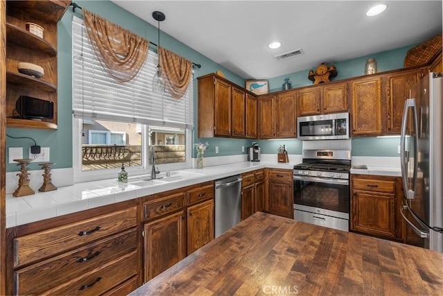 kitchen featuring stainless steel appliances, tile countertops, hanging light fixtures, and sink