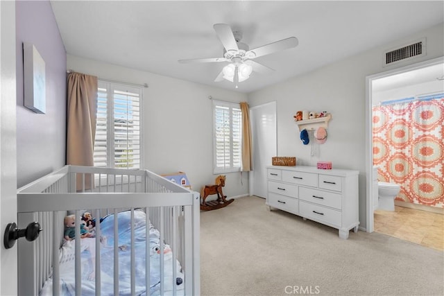 carpeted bedroom featuring ceiling fan, a nursery area, and ensuite bathroom