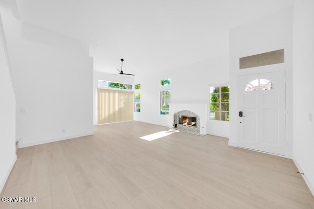 unfurnished living room featuring light wood-type flooring, ceiling fan, and a high ceiling