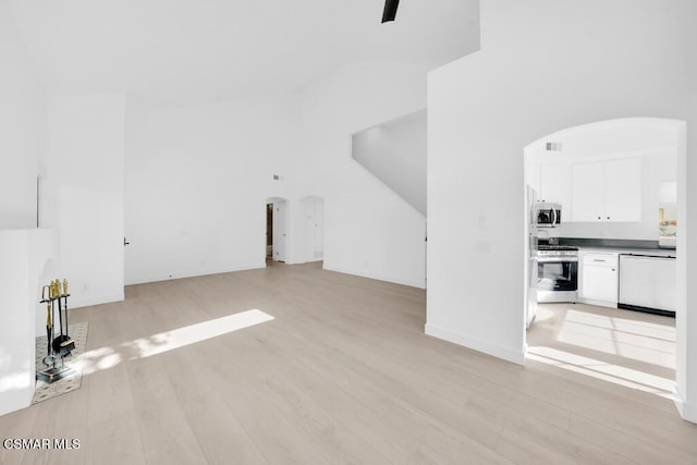 unfurnished living room featuring ceiling fan, light wood-type flooring, and a towering ceiling