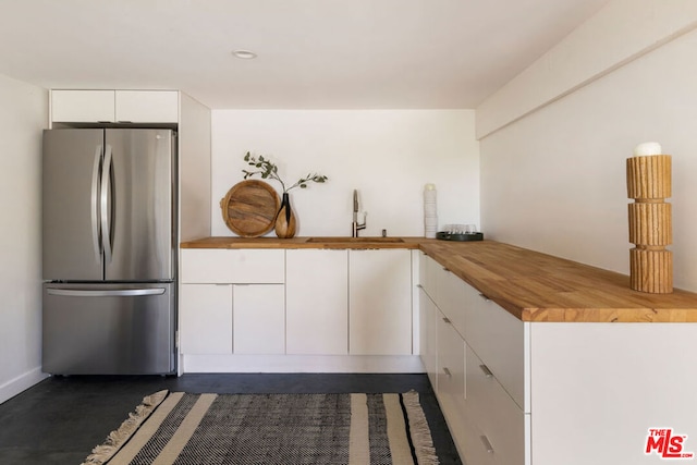 kitchen featuring wood counters, white cabinetry, stainless steel fridge, and sink