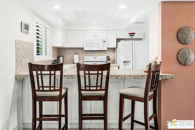 kitchen with white cabinetry, a kitchen bar, kitchen peninsula, a raised ceiling, and white appliances