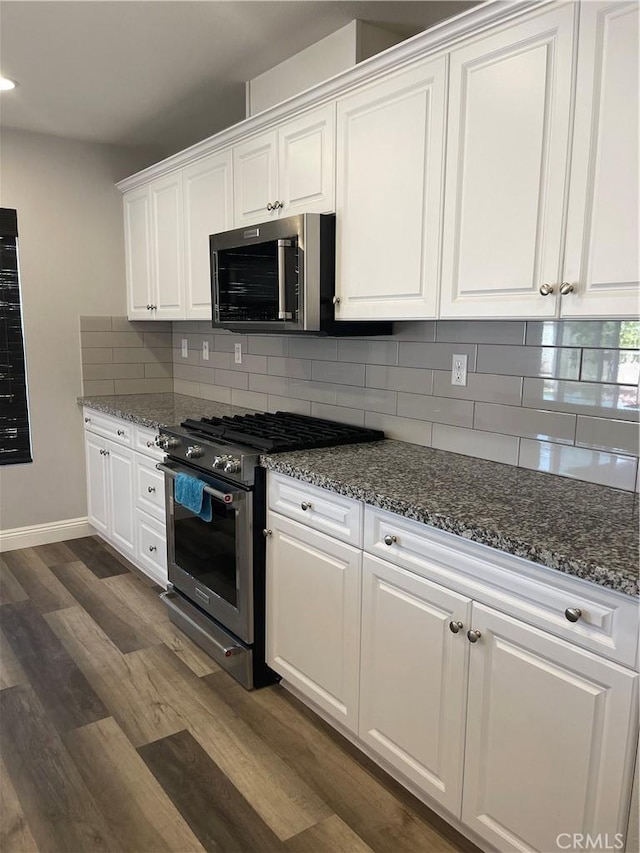 kitchen with appliances with stainless steel finishes, dark wood-type flooring, white cabinetry, dark stone counters, and decorative backsplash