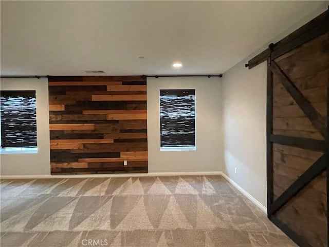 carpeted empty room featuring a barn door, wooden walls, baseboards, and recessed lighting