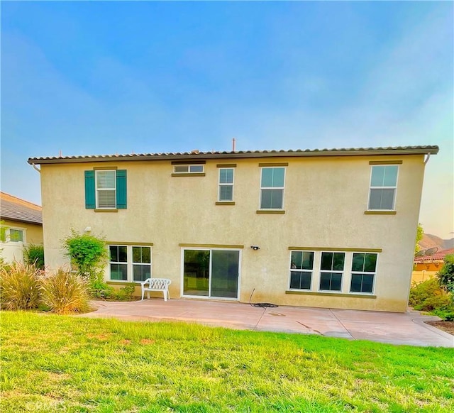 back of property with a yard, a patio area, and stucco siding