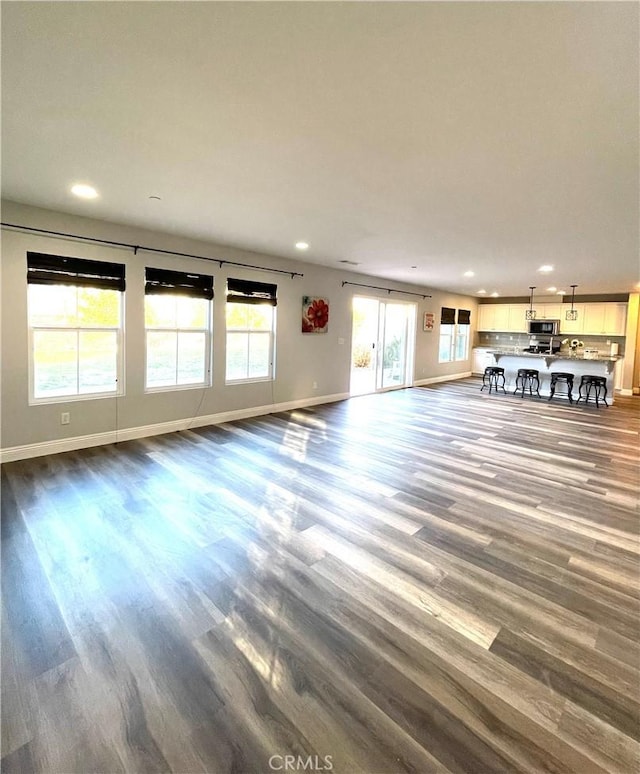 unfurnished living room featuring recessed lighting, plenty of natural light, baseboards, and wood finished floors