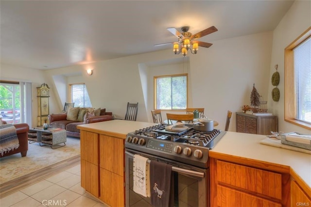 kitchen featuring ceiling fan, a wealth of natural light, stainless steel range with gas stovetop, and light tile patterned flooring