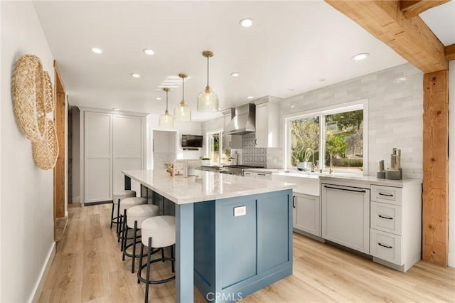 kitchen featuring decorative light fixtures, wall chimney range hood, a large island, light hardwood / wood-style floors, and paneled dishwasher