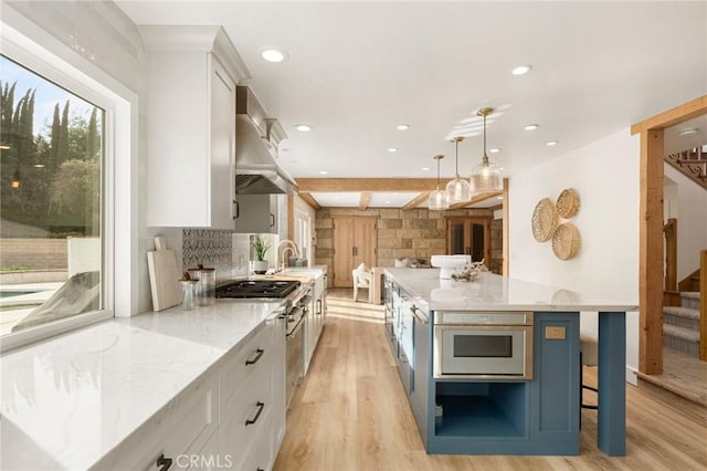 kitchen featuring hanging light fixtures, white cabinetry, ventilation hood, and light stone counters